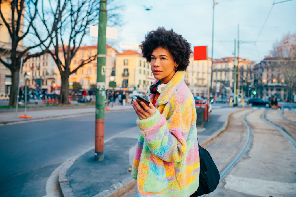 Young black smiling woman traveler using smartphone outdoor sightseeing carrying duffle bag